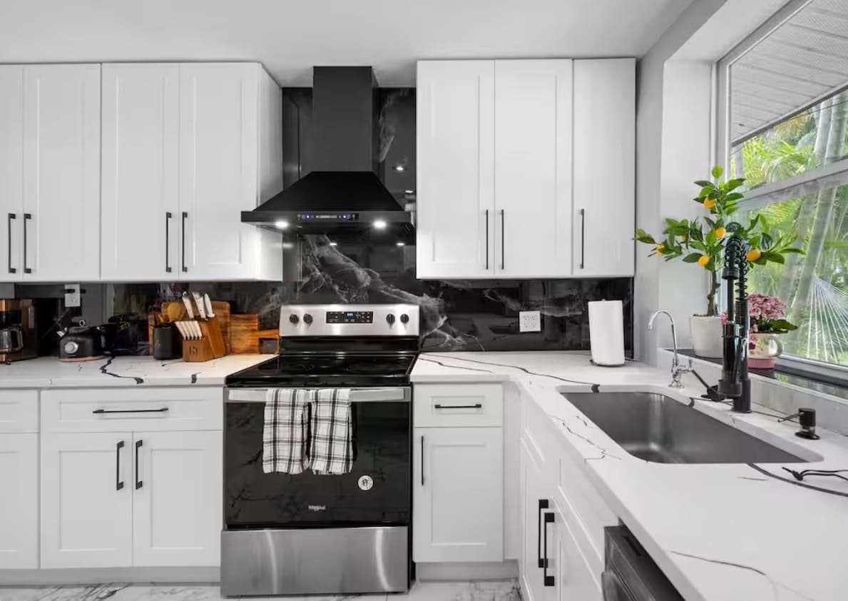 Finished kitchen remodel with white cabinetry, stainless appliances and marble-look flooring — REV Home Solutions