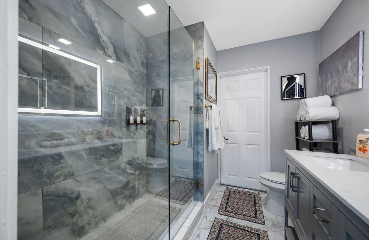 Custom glass shower enclosure with marble-look tile — REV Home Solutions