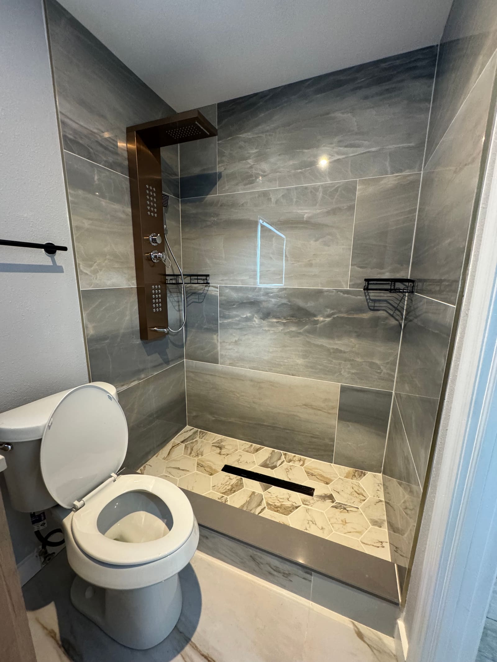 Finished walk-in shower with gray stone tile walls and marble hexagon floor tile — REV Home Solutions